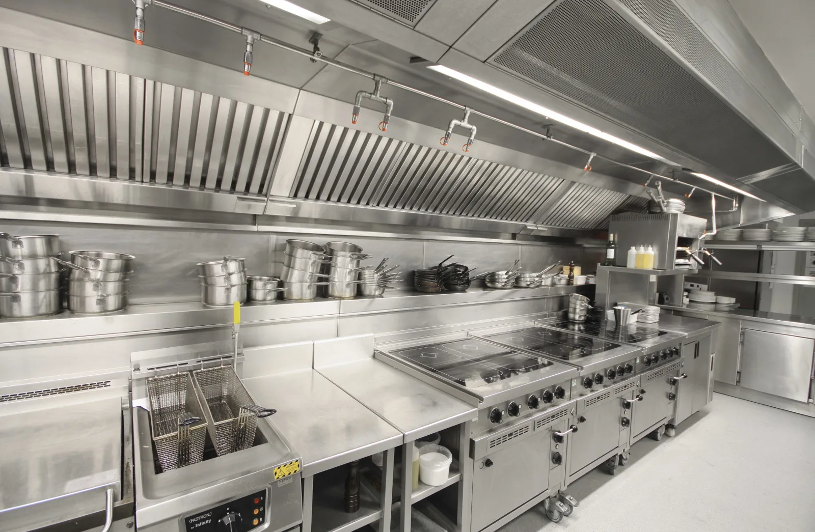 Long stainless steel exhaust hood above a commercial kitchen cooking line with fryers and ranges