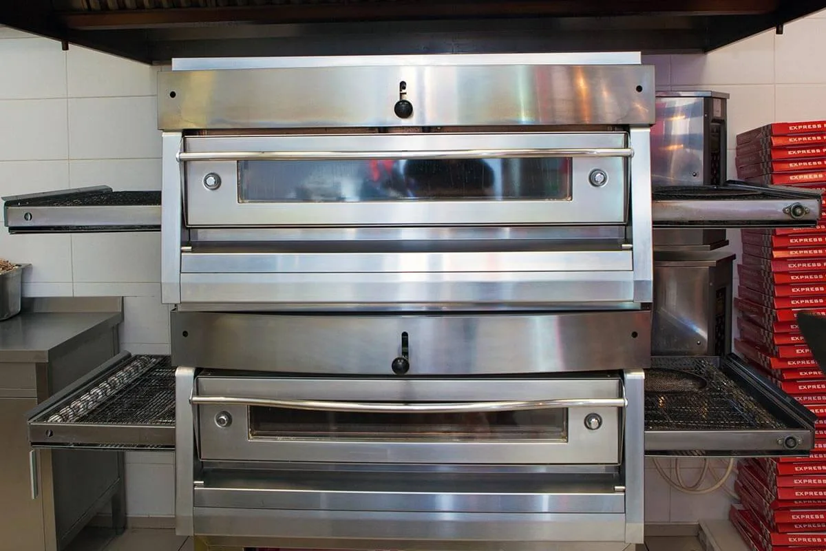 Cleaned stainless steel commercial conveyor pizza ovens stacked in a restaurant kitchen