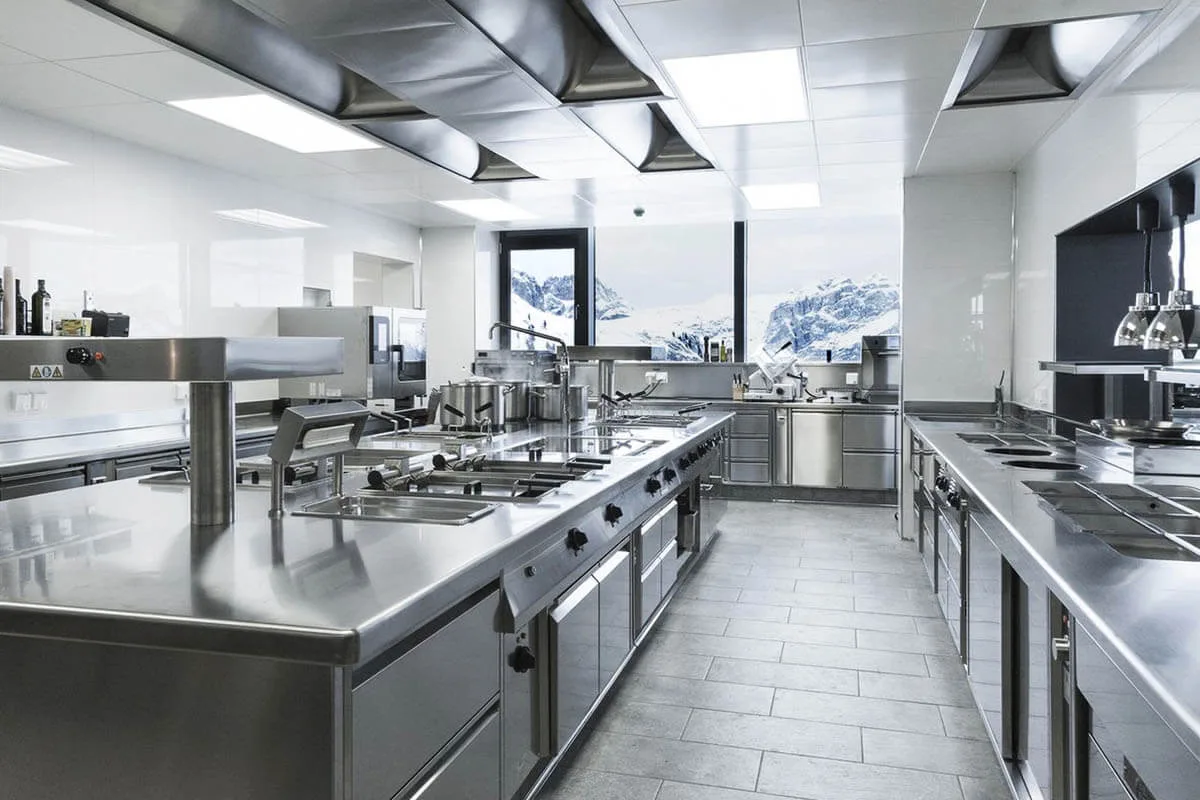 Spotless stainless steel commercial kitchen with ranges and prep tables after deep cleaning